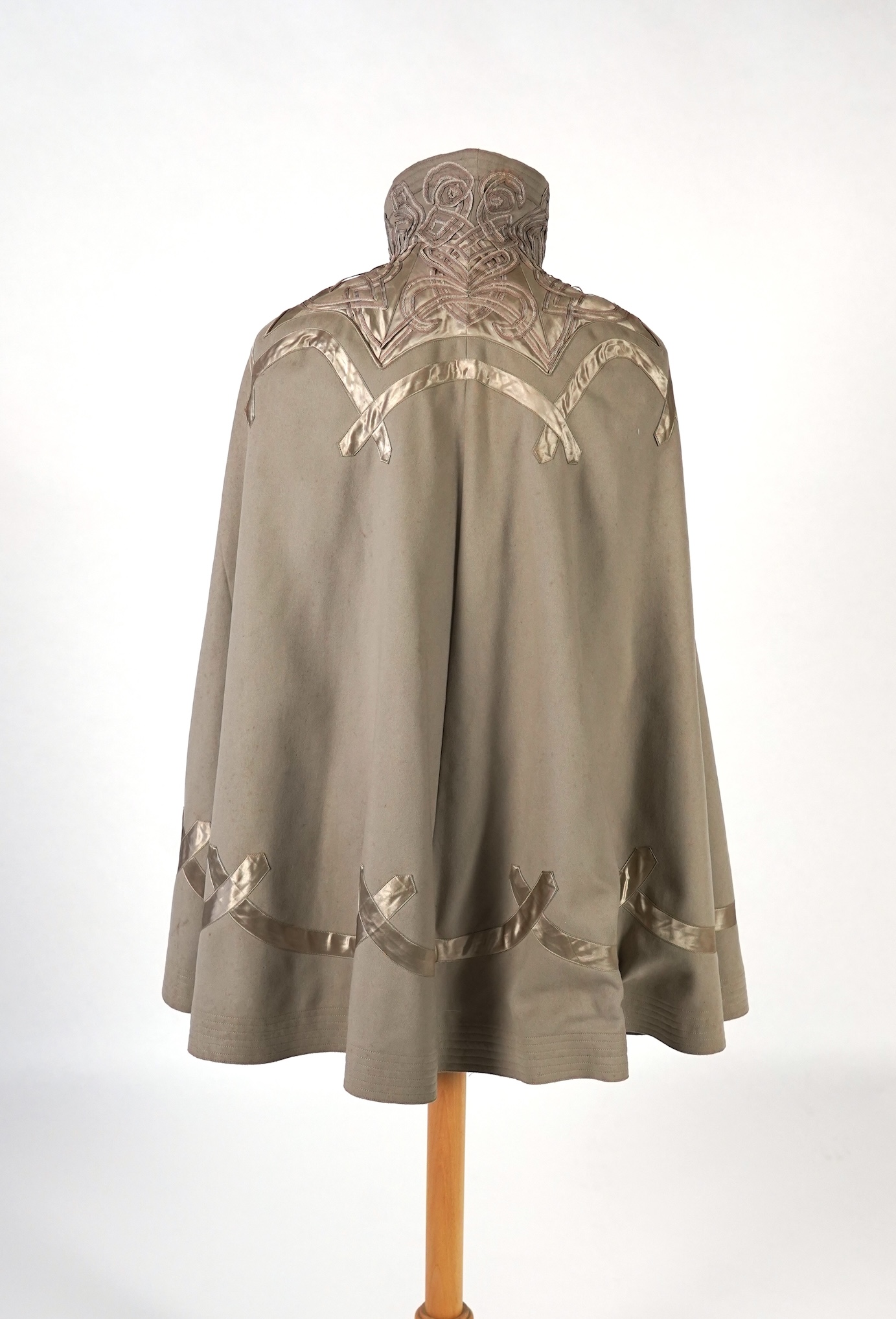 An Edwardian mushroom wool evening cape, decorated with silk ribbon worked strapping and ornate appliquéd fine braiding across the shoulders and under section of the collar, lined with cream silk satin.